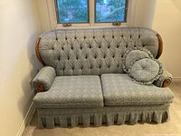 Front view of the loveseat showing tufted upholstery, wooden arms, skirt, and pillows