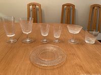 Overview of crystal glasses and a dessert plate on wooden table against chairs