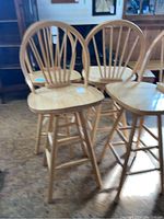 Four matching maple swivel bar stools with backs, arranged in a group showing front and side profile under natural lighting.