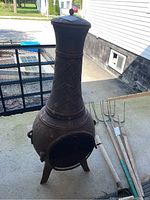 Full view of cast iron chiminea showing its height, shape, mesh door in front, and diamond patterned chimney with rust.
