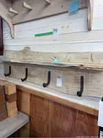 Wooden coat rack with a long wood rail and five black metal hooks, showing length and placement on a white wooden wall.