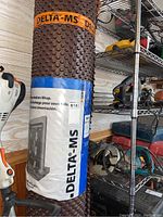 Photo showing rolled Delta-MS Foundation Wrap with brown dimpled surface and white product label with blue accents.