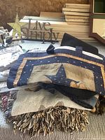 Pile of homespun textiles including table runners, valance or wall hanging with star and heart appliqué, and a large fringed throw.