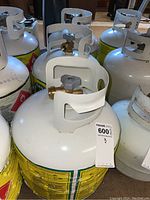 Photo of three propane tanks showing white body, yellow and green Tank Traders labels, and brass valves with gray handles.