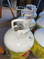 Photo of three white propane tanks with yellow and green label, showing valve and protective collar on top