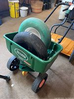 Full view of the green Scotts SpeedyGreen 3000 seeder showing the plastic hopper and wheels with the two trailer tires placed inside the hopper for display.