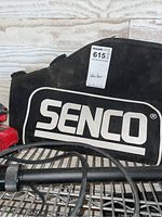 Photo of the Senco soft carrying case with large white brand logo, showing part of the nailer and cable inside.