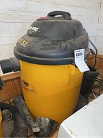 Shop Vac unit showing yellow drum body, black lid, and attached hose and accessories visor.