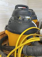 Yellow and black Vac n Vac Shop Vac wet/dry vacuum with handle and hose attached. Shows signs of use and dust.