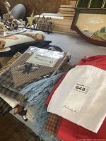Multiple homespun valances, packaged and loose, along with tea towels and a red cloth, displayed on table