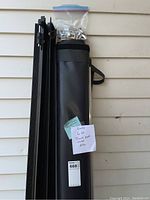 Soft rolled-up black tonueau cover with attached black strap, standing vertically with mounting frame.