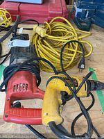 Three items on wooden surface: Dewalt yellow drywall screwdriver DW252 with label visible, red reciprocating saw, yellow extension cord coiled.