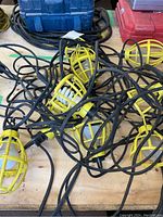 Overview photo showing a tangled set of nine yellow protective cage trouble lights with black cords on a wooden surface.