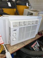 White Arctic King window air conditioner with front control panel and adjustable side panels on a workbench.
