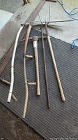Photo showing six yard tools including two scythes, pitchfork, edging tool and pickaxe on a black rubber mat.