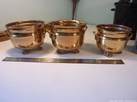 Three graduated brass planters lined up side by side with a ruler for size reference