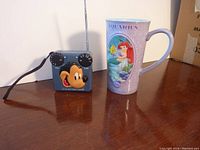 Full view of the vintage Mickey Mouse radio and Ariel Disney grande mug on a wooden surface