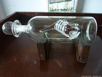 Side view of the glass bottle with the glass ship inside, displayed on two wooden stands.