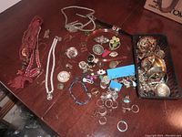 Wide view of assorted jewelry pieces scattered on table showing necklaces, earrings, rings, bracelets, headband, and pins.