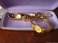 Four ladies wristwatches displayed inside a purple jewelry box, featuring metal bands and varied round faces in gold and silver tones.