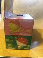 Side view of sealed box showing boomerang and stair descending features of the Wizzzer toy.