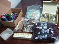 A wide view of assorted sewing supplies including thread spools, wool, buttons, sewing machine attachments, and storage boxes on a table.