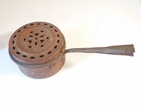 Copper pot viewed from the side showing the lid with cutouts and long straight handle