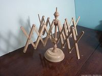 Front and side view of expandable wooden wool winder set to full width on a dark wood surface with a light blue wall behind.