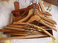 Photo showing a wooden box containing multiple wooden hangers with metal hooks. Some hangers have printed store names or logos visible.