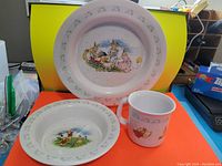 Set of three Bunnykins ceramic tableware items: plate, bowl, cup with character designs and bunny border