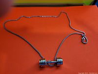 Photo of a silver-tone stainless steel chain necklace with a dumbbell pendant lying flat on an orange surface.