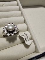 Close-up photo of a sterling silver adjustable ring with a flower shaped rhodium setting and genuine cultured pearl in the center. Original price tag visible.
