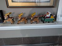 Full view of handmade wooden Santa Claus in a sleigh pulled by three wooden reindeer on a white base, showing colors, details, and proportion.