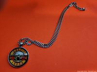Black chain necklace with a round glass cabochon pendant showing the Guns N Roses logo on an orange background.