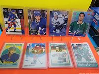 Eight NHL rookie hockey cards displayed on a yellow and orange stand, six in soft plastic sleeves, two in hard plastic holders. Cards feature various players and rookie card designs from multiple years.
