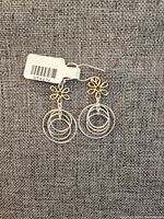 Photo of a pair of two-tone sterling silver earrings with intertwined three-circle drop design and delicate gold-tone flower base on a fabric background.