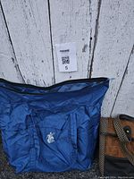 Blue nylon duffle bag with front pocket and zipper closure, shown against white wood background