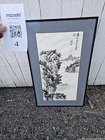 Full view of framed Chinese landscape art print showing the entire artwork and frame propped against a wall outdoors.