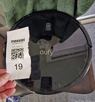 Top view image of the Eufy robotic vacuum cleaner showing the power button and branding with hand holding a ticket