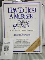Front of the game box showing title 'How To Host A Murder: Hoo Hung Woo' with theatrical mask graphics and some age spots on box surface.