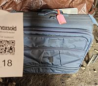 Front view of blue fabric suitcase with multiple zippered pockets and a red luggage tag attached to the handle.