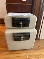 Two stacked Sentry safes, beige with black lock handles and keys in both locks, on a wooden floor.