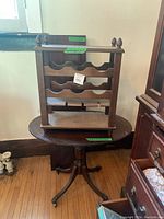 Side view of the small oval antique wooden side table with splayed legs and metal caps showing the wine rack placed on top.