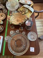 View of assorted glassware and serving pieces on wooden table showing candy bowl, candlesticks, cookie jar, and glass plates.