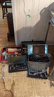 Photo showing three toolboxes on the floor, two metal and one red plastic, containing assorted hand tools and socket set cases