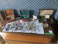 Overview photo of the assortment spread out on a table showing three wooden jewelry boxes and a variety of colorful costume jewelry including brooches, earrings, and cufflinks.