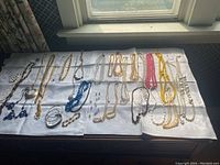 Wide shot of assorted costume jewelry laid on a white cloth, showing multiple necklaces, bracelets and a few pairs of earrings of various colors and styles.