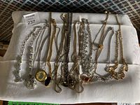 Assortment of costume jewelry necklaces and chains in silver and gold tones displayed on white cloth