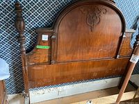 Photo of the carved wooden headboard with rounded top and finials, showing medium brown wood and decorative design