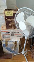 Photo showing the standing oscillating fan and stacked boxed toaster oven and blender with visible wear on packaging.